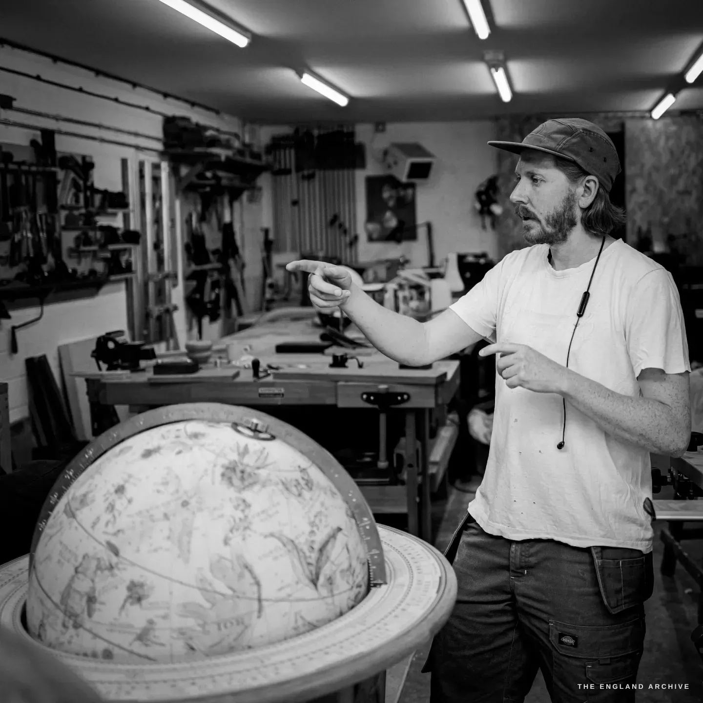 Louis gesturing as he talks, a hand-illustrated celestial globe on its stand in the foreground, his woodworking shop behind.