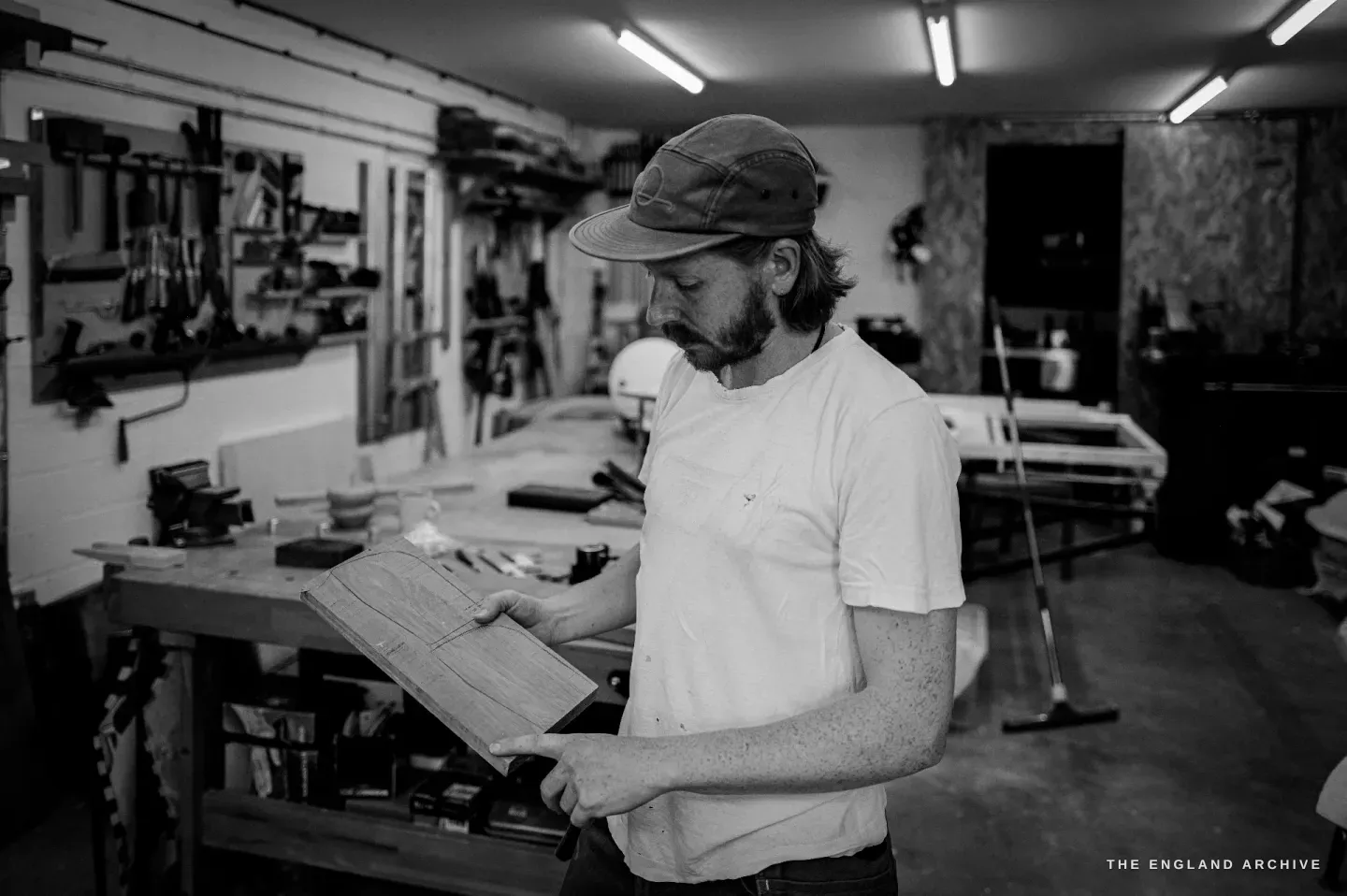 Louis holding a board up to read its grain, the tool wall and vice behind him.