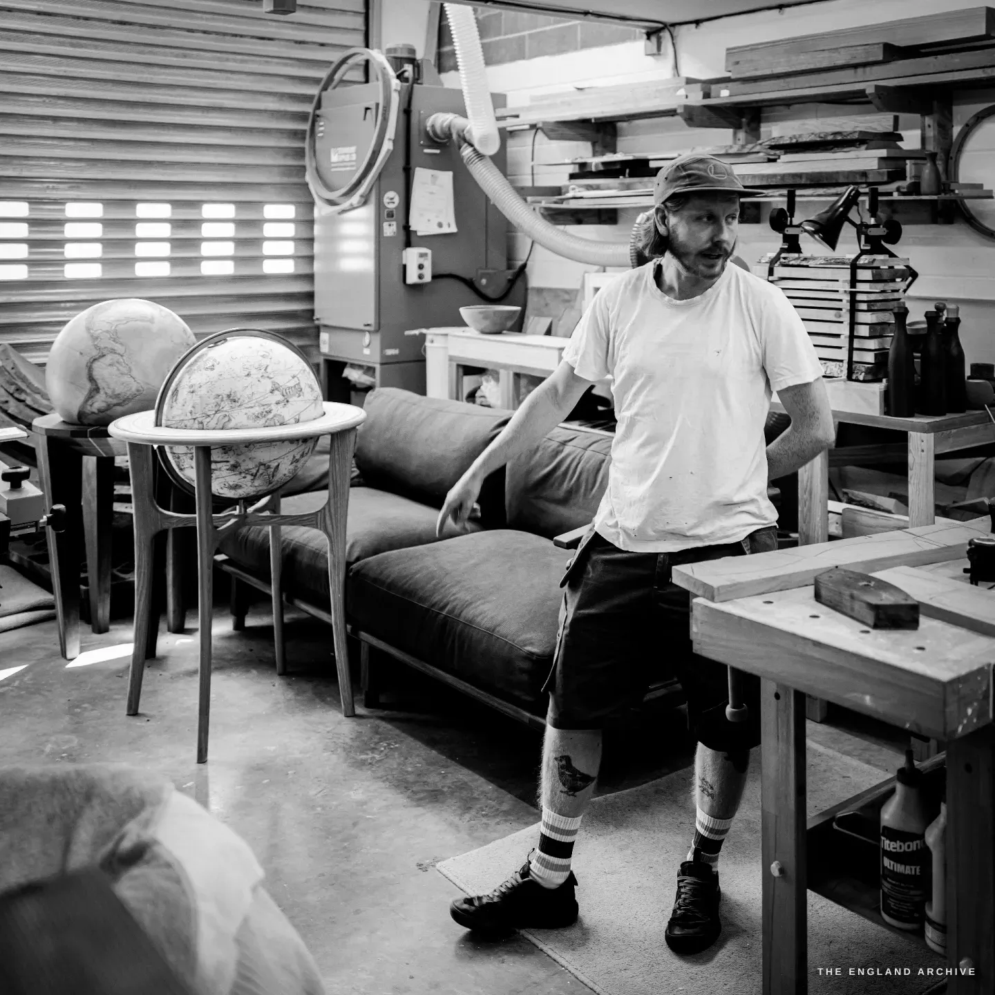 Louis leaning against a workbench in his workshop, a celestial globe on a stand to one side, turned vessels and timber around him.