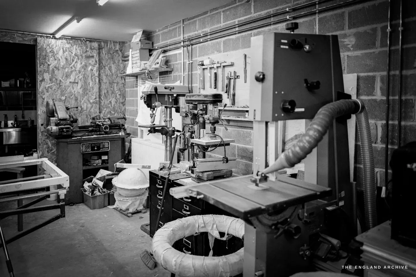 The machine corner of the woodshop - a lathe, pillar drill and bandsaw with dust extraction, timber stacked against the wall.