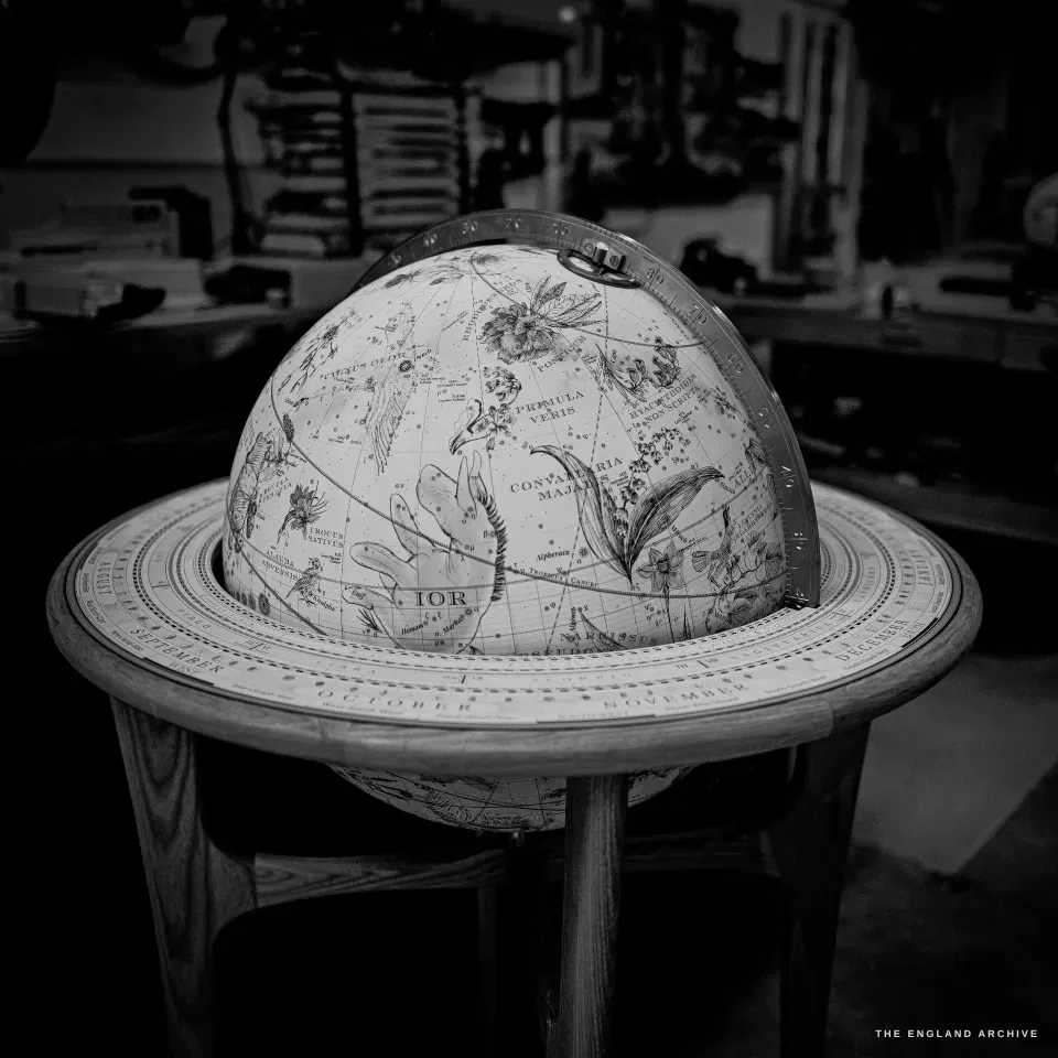 A hand-illustrated celestial globe set in a pale wooden stand with a broad calendar horizon ring and a brass meridian.
