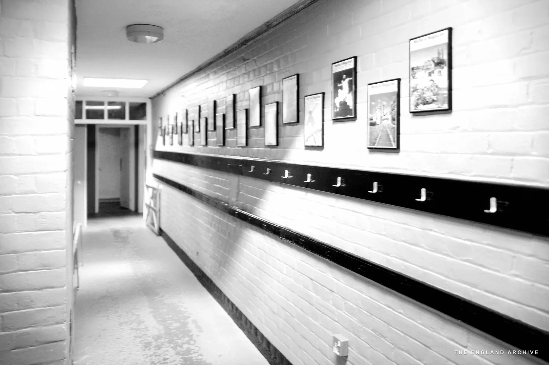 Pink-painted brick corridor with coat hook rail and framed children's artwork along the wall, Old School interior.