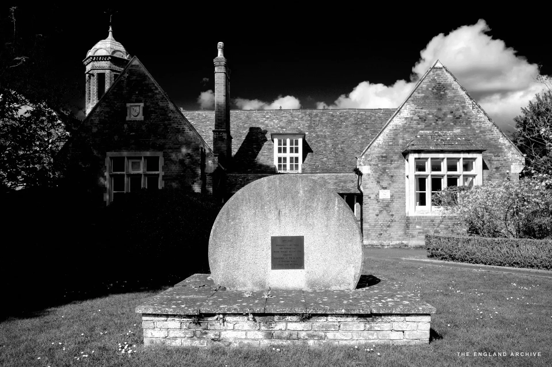 A stone memorial ball on a plinth in front of the Old School's Victorian red brick facade.