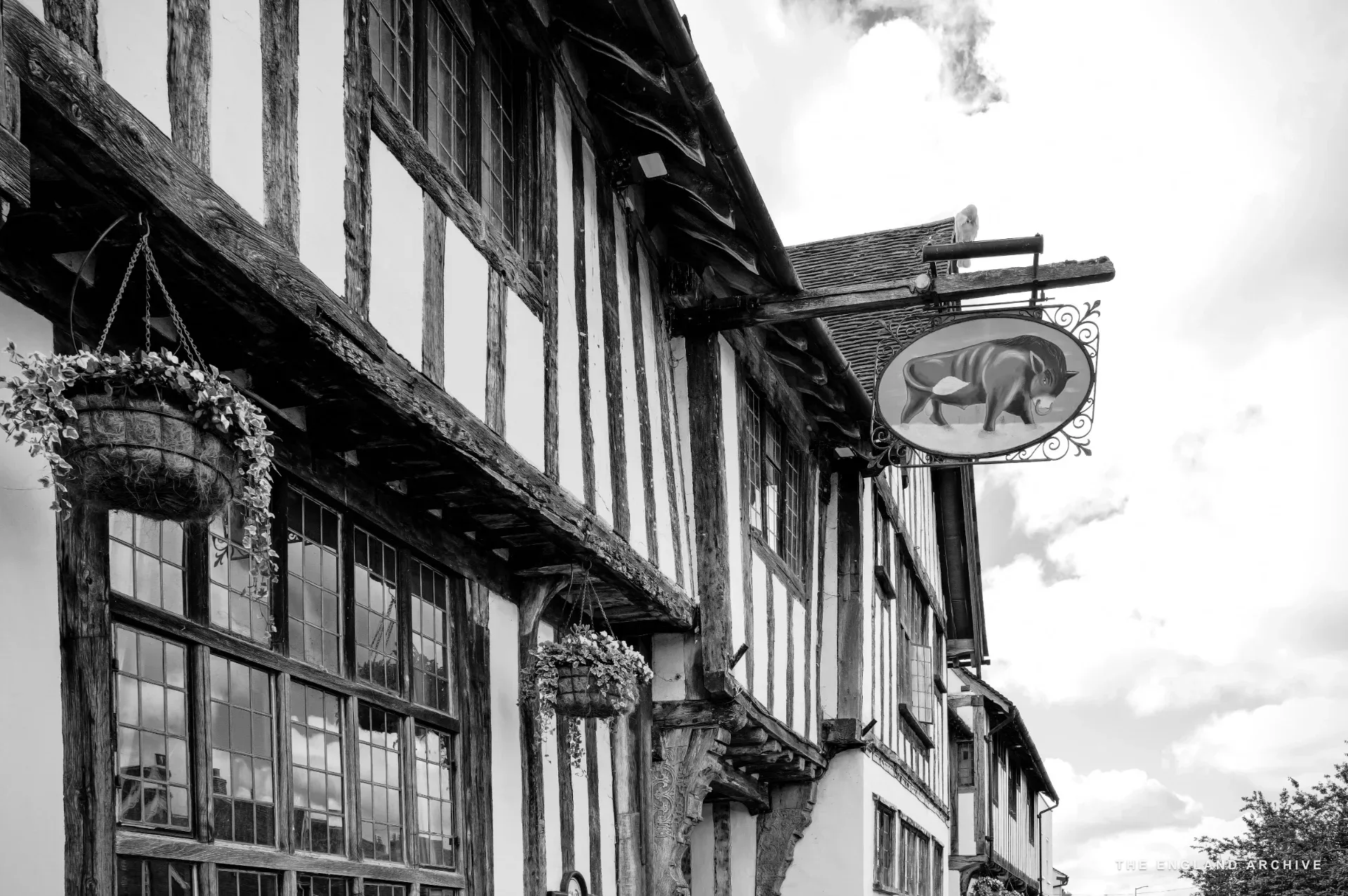 The Bull Hotel's Tudor timber-framed frontage with hanging flower baskets and a painted pub sign.