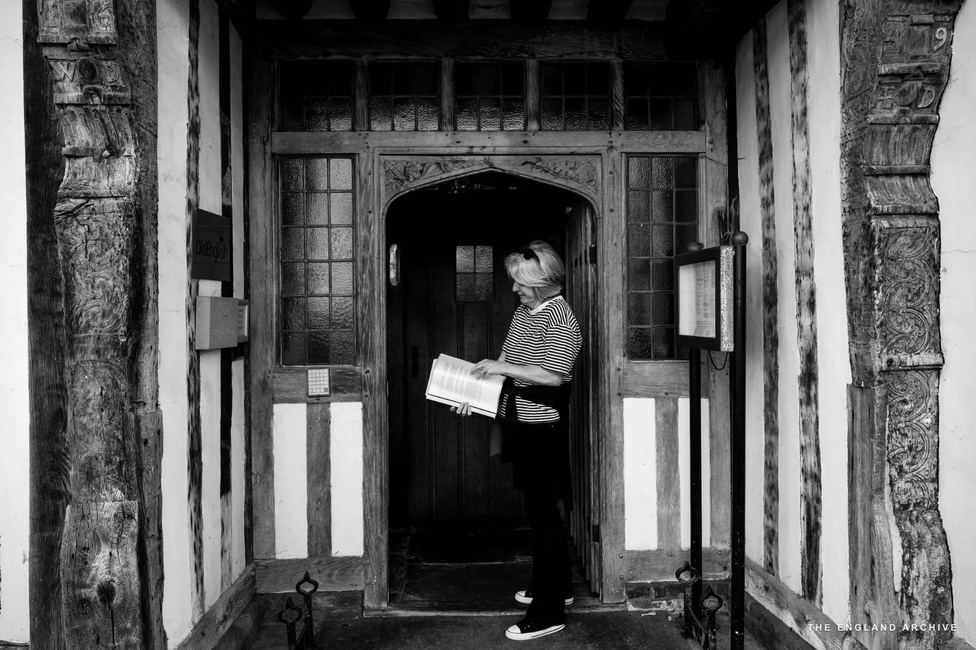 Julie Thomson reading a leaflet in a Tudor doorway with a carved timber surround.