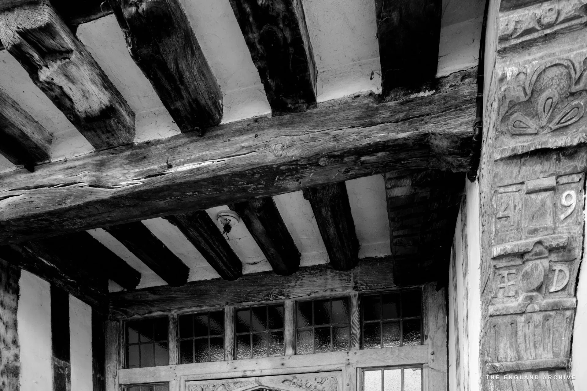A close view of heavy Tudor roof beams and a carved stone doorway surround showing the number '9' and floral motifs.