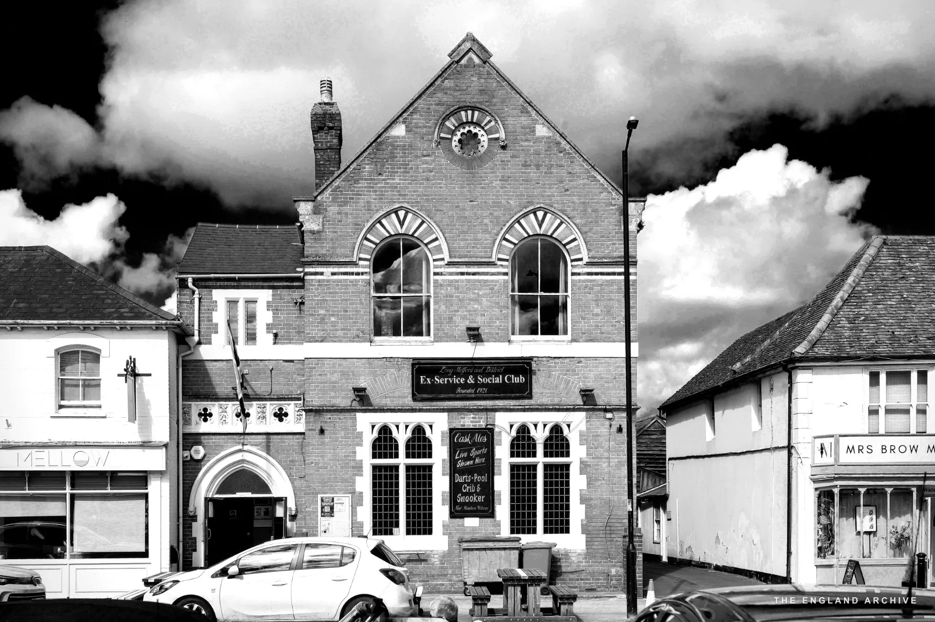 The 'Oldspeak Bookshop' with white arched windows, a Union Jack, a red door, and an outdoor clothes rail.