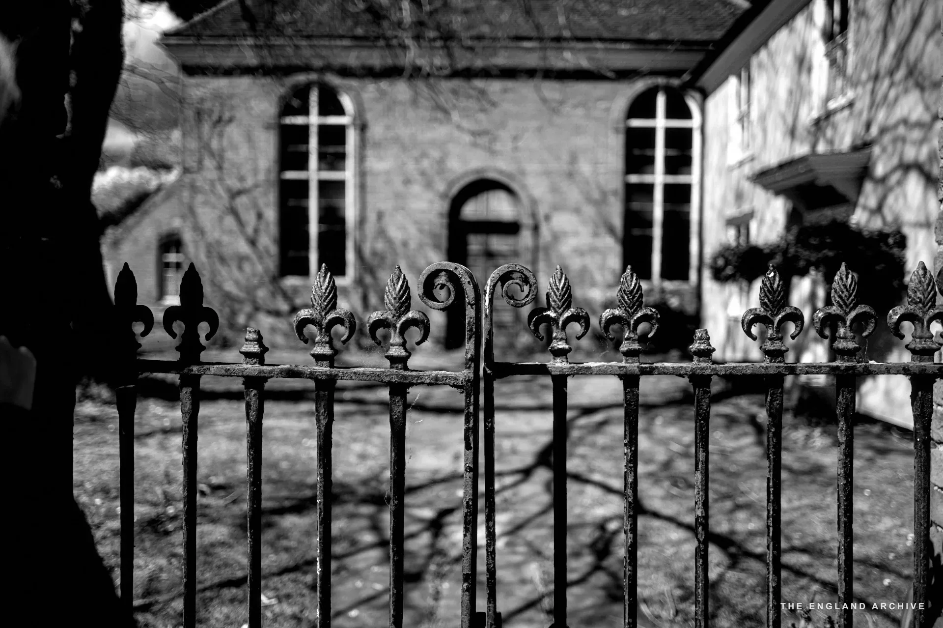 Wrought-iron railings with fleur-de-lis finials in the foreground, the chapel blurred behind.