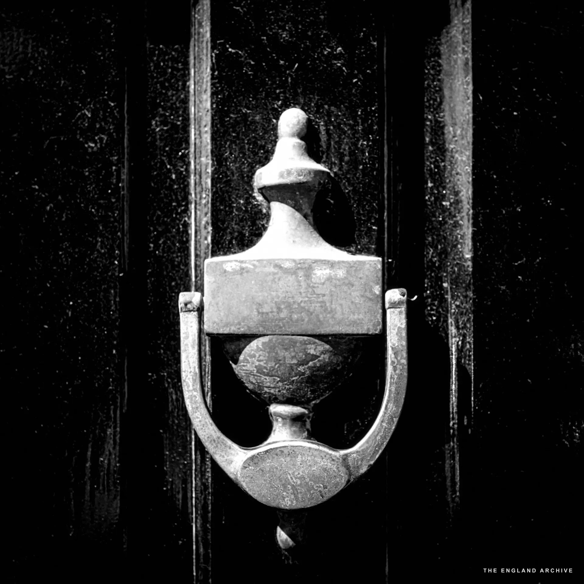 A tight close-up of a weathered verdigris and brass urn-shaped door knocker on a black-painted door.