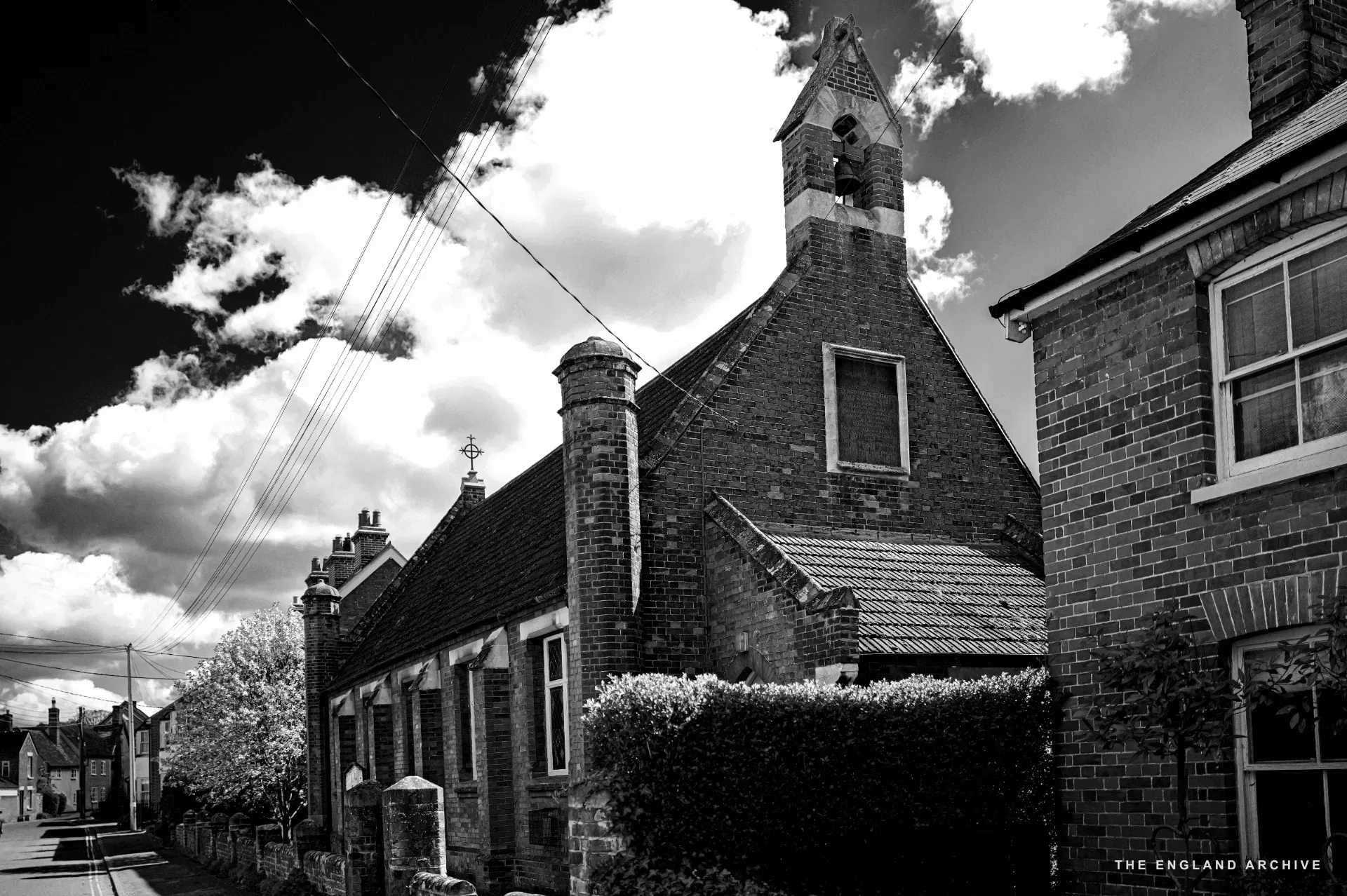 A red-brick Victorian chapel with a bellcote and arched windows beside a residential lane.