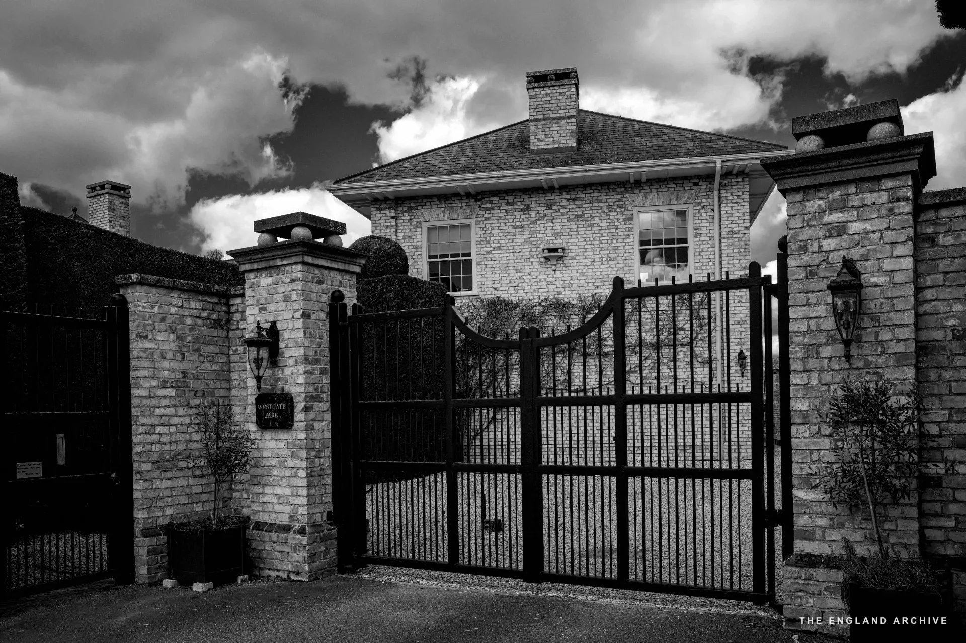 Ornate black wrought-iron gates between brick piers leading to a grand yellow-brick country house with tall chimneys - the Edwards estate.