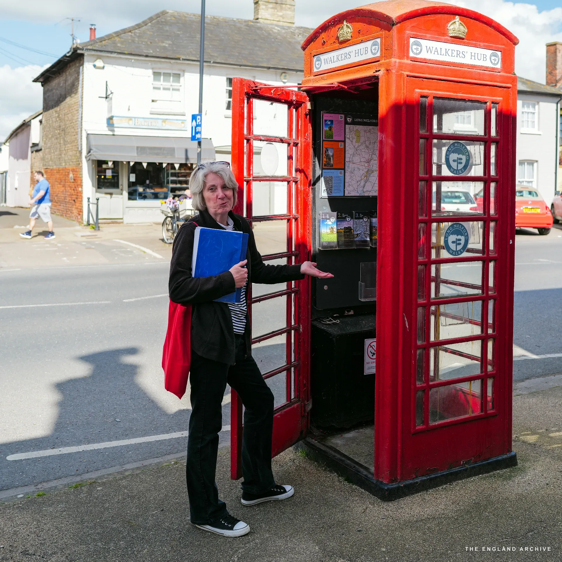 A carved wooden cigar-store figure in a red and yellow headdress standing beside the doorway of a 'Premium Cigars' shop, a man in a trilby hat holding a cigar at the door.