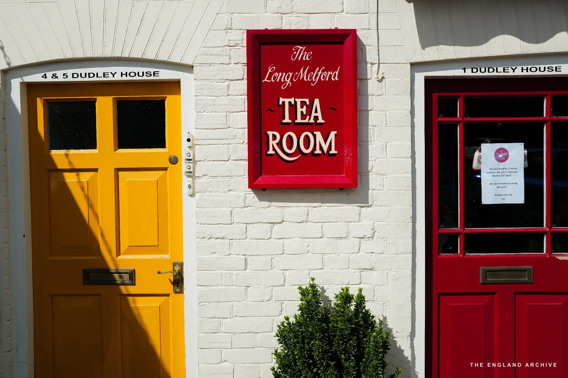 The yellow door of '4 &amp; 5 Dudley House' on the left and the red door of '1 Dudley House' on the right, with the red tea room sign between on the white wall.