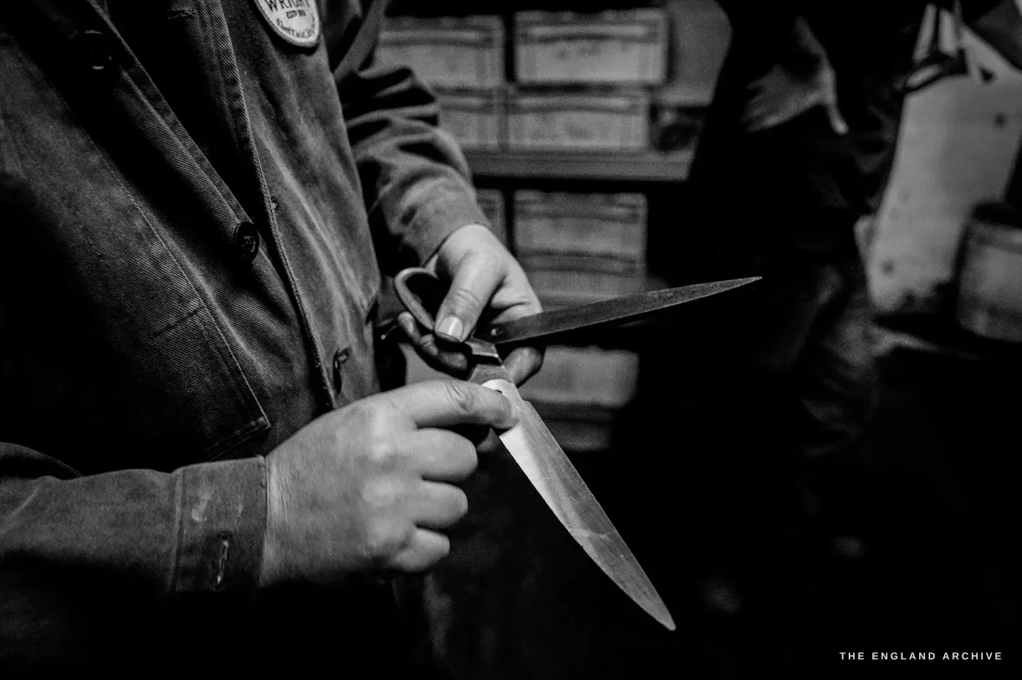 Neil holding a large open pair of scissors in both hands, sighting along the two blades to check how they meet.