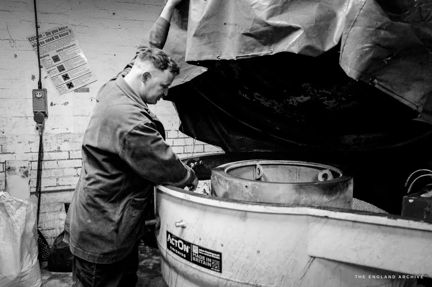 Neil leaning over a large round drum machine, the rumbler, lifting its heavy cover to check the scissors inside.