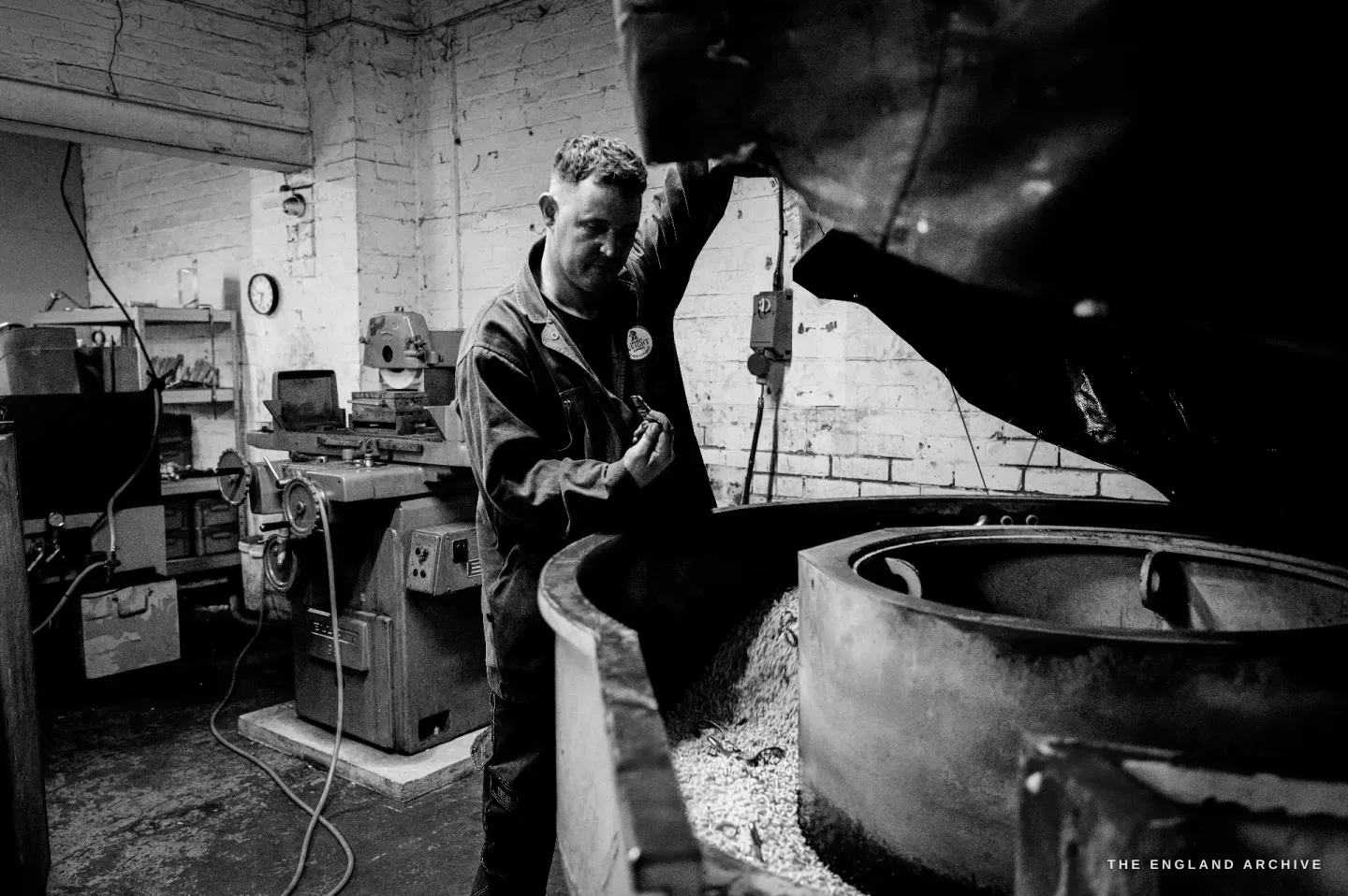 Neil working at the open rumbler, the ceramic media and parts visible in the drum, finishing machines along the wall behind.