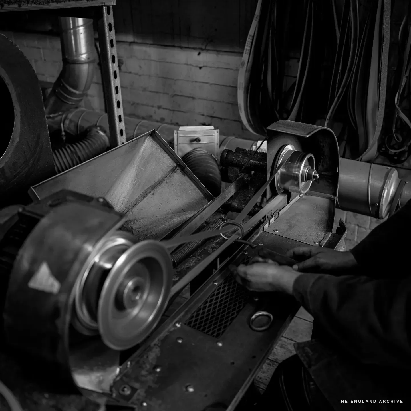 A close view of a grinding wheel on its mandrel as a blade is worked against it, the belt-driven machinery dark around it.