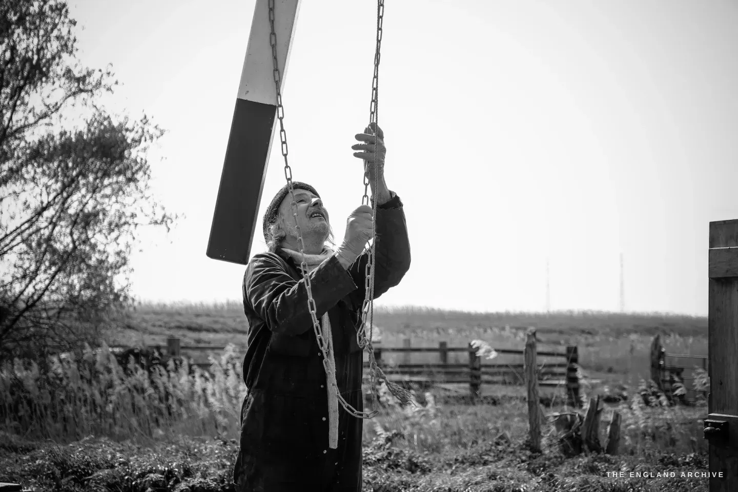 Paul pulling the chain to release the brake, looking up, the marshes behind him
