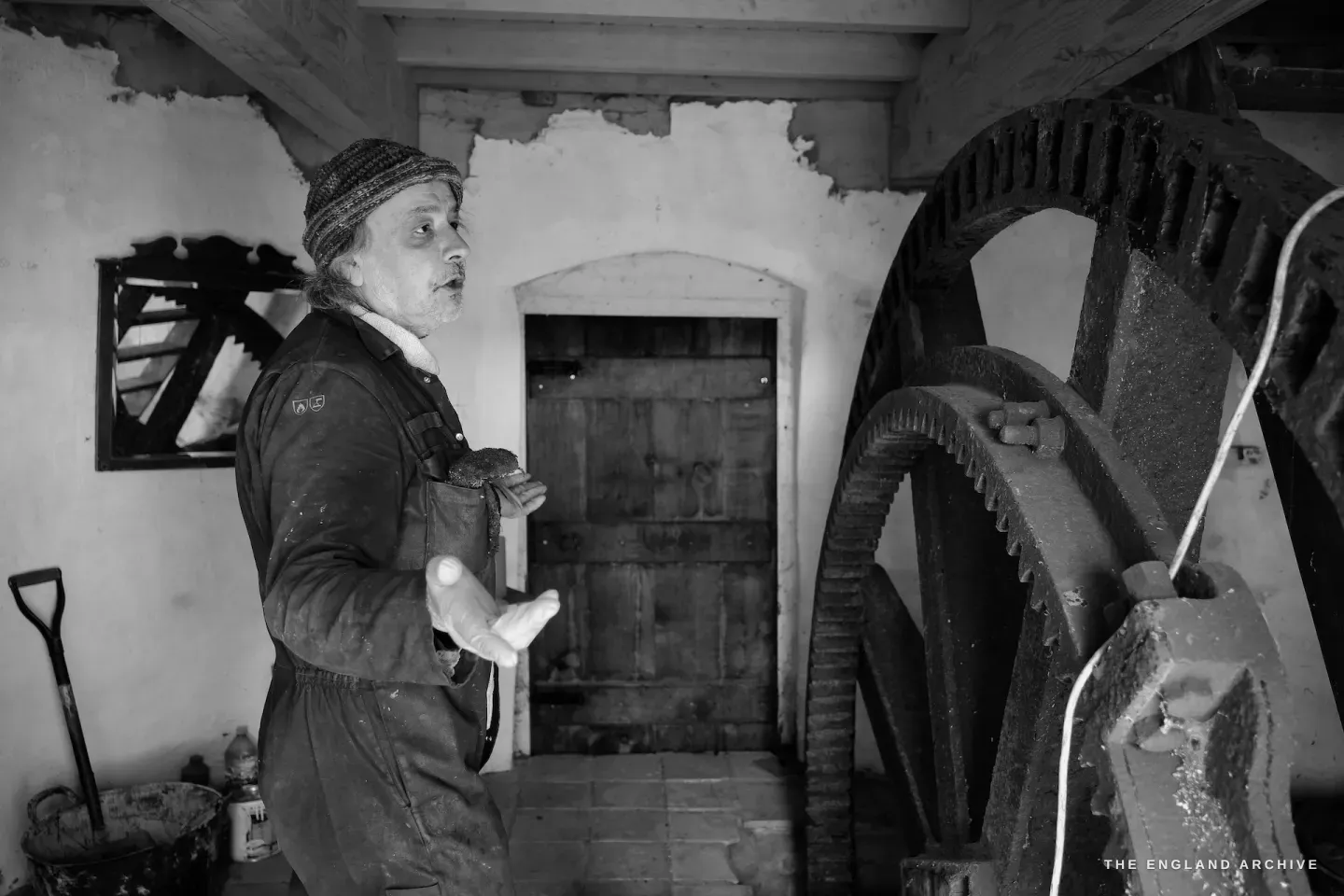 Inside Toft Monks Mill - Paul beside the large gear wheel, gesturing as he explains how the mechanism works
