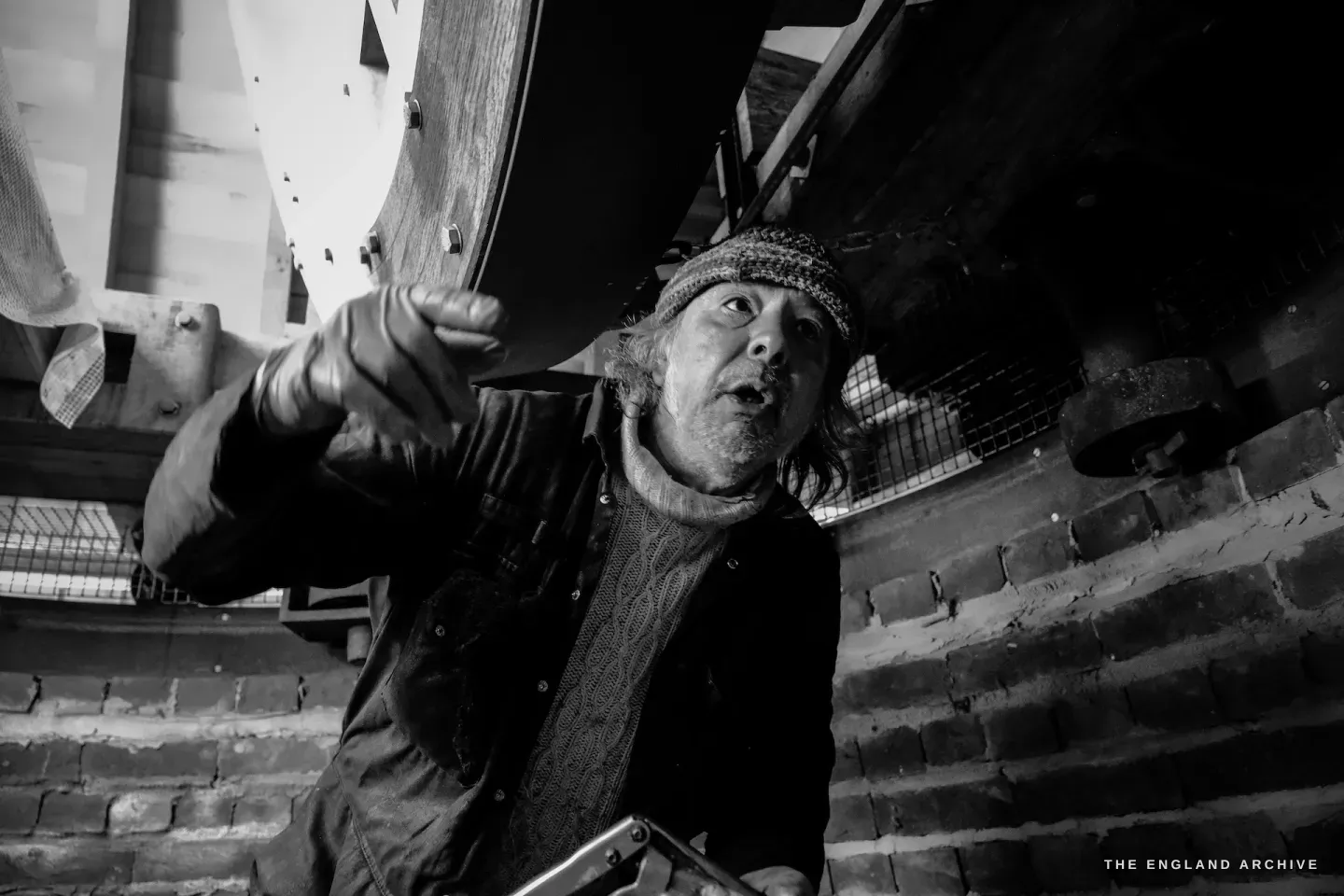 Paul inside the mill pointing upward emphatically, face animated, explaining the mechanism