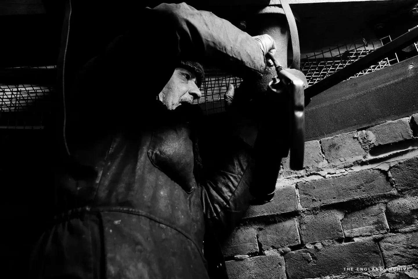 Paul in dramatic side-light inside the mill, profile silhouetted against the brickwork, deep shadow and texture