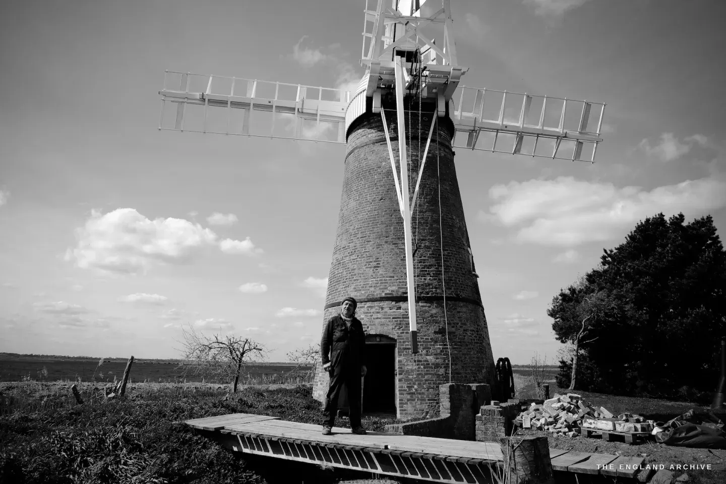 Paul Kemp standing at the mill door, hands at his sides, the flat Norfolk landscape behind him