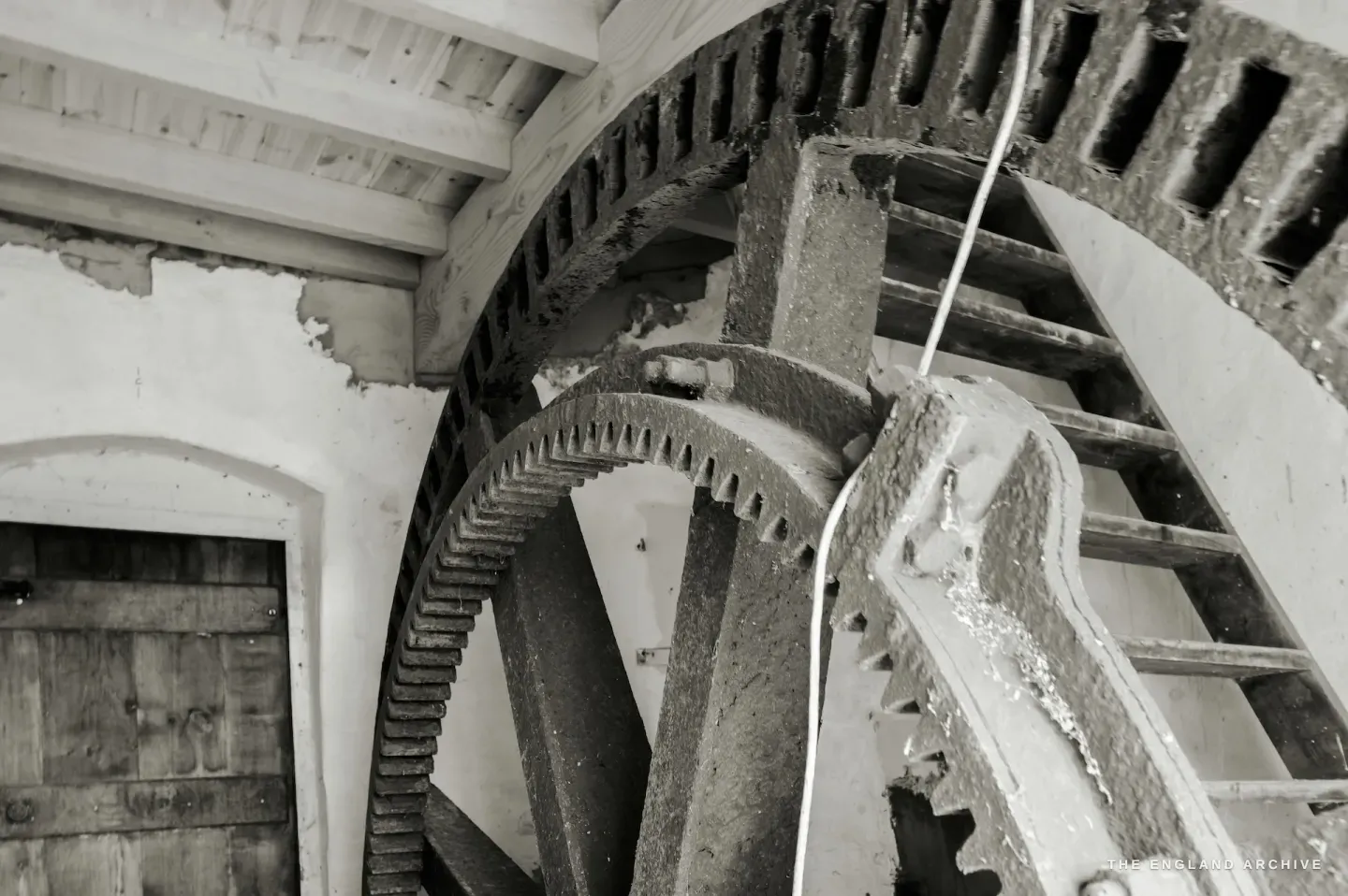 The gear mechanism from a different angle, the doorway visible behind, timber beams and plaster walls