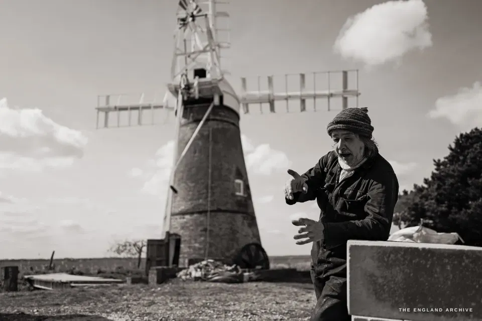 Paul gesturing with both hands, the mill behind him, explaining something about the engineering