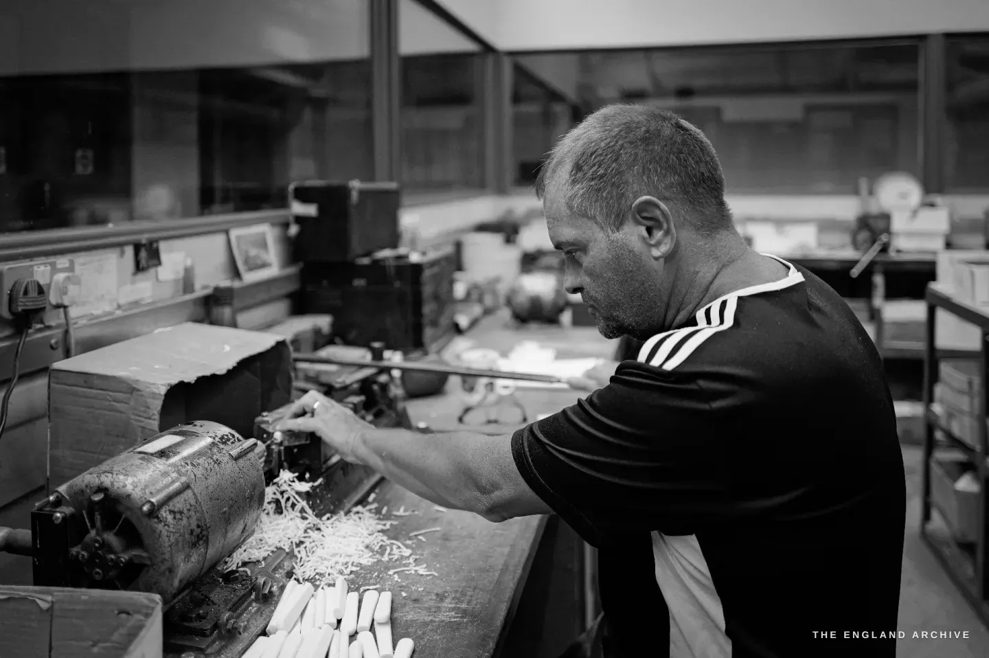 Paul bent over a drilling machine working into a handle, a scatter of pale cream handle blanks on the bench below.