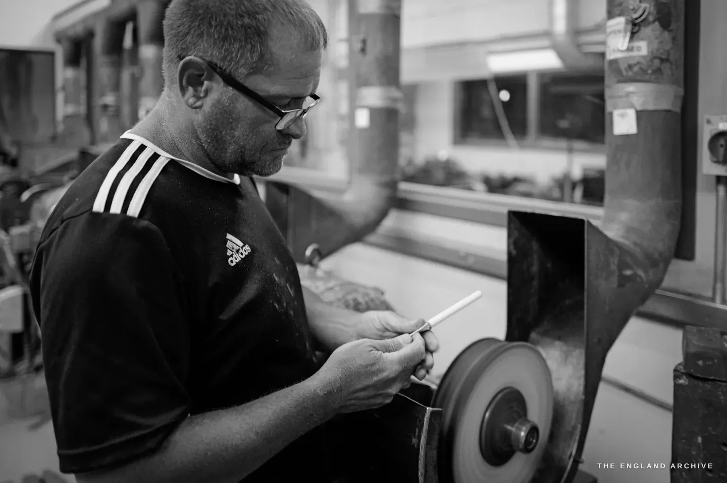 Paul holding a pale handle to a wheel, head down in concentration, the finishing room stretching away behind.