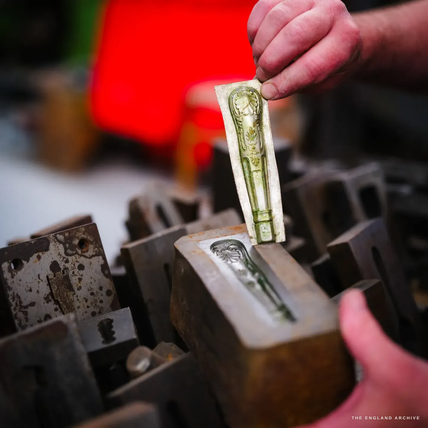 A close view of two hands lowering a relief-cast handle pattern into the matching cavity of an iron flask, nested among many other mould blocks.