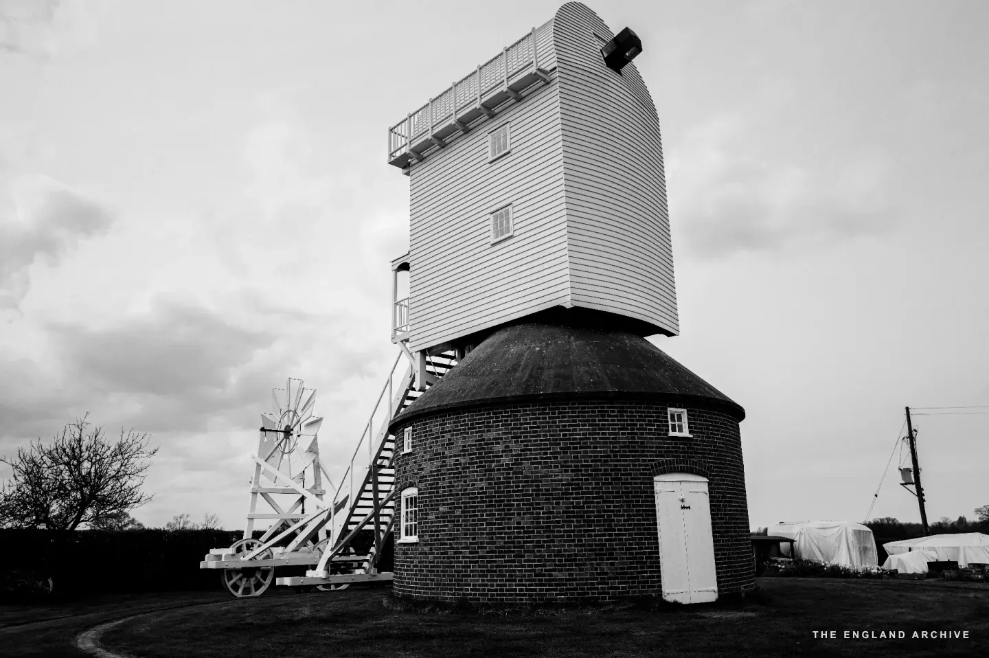 The post mill at South Walsham viewed three-quarters from the front: a circular brick roundhouse below, a white-clapboard upper body above, the long wheeled fantail extending to the right.