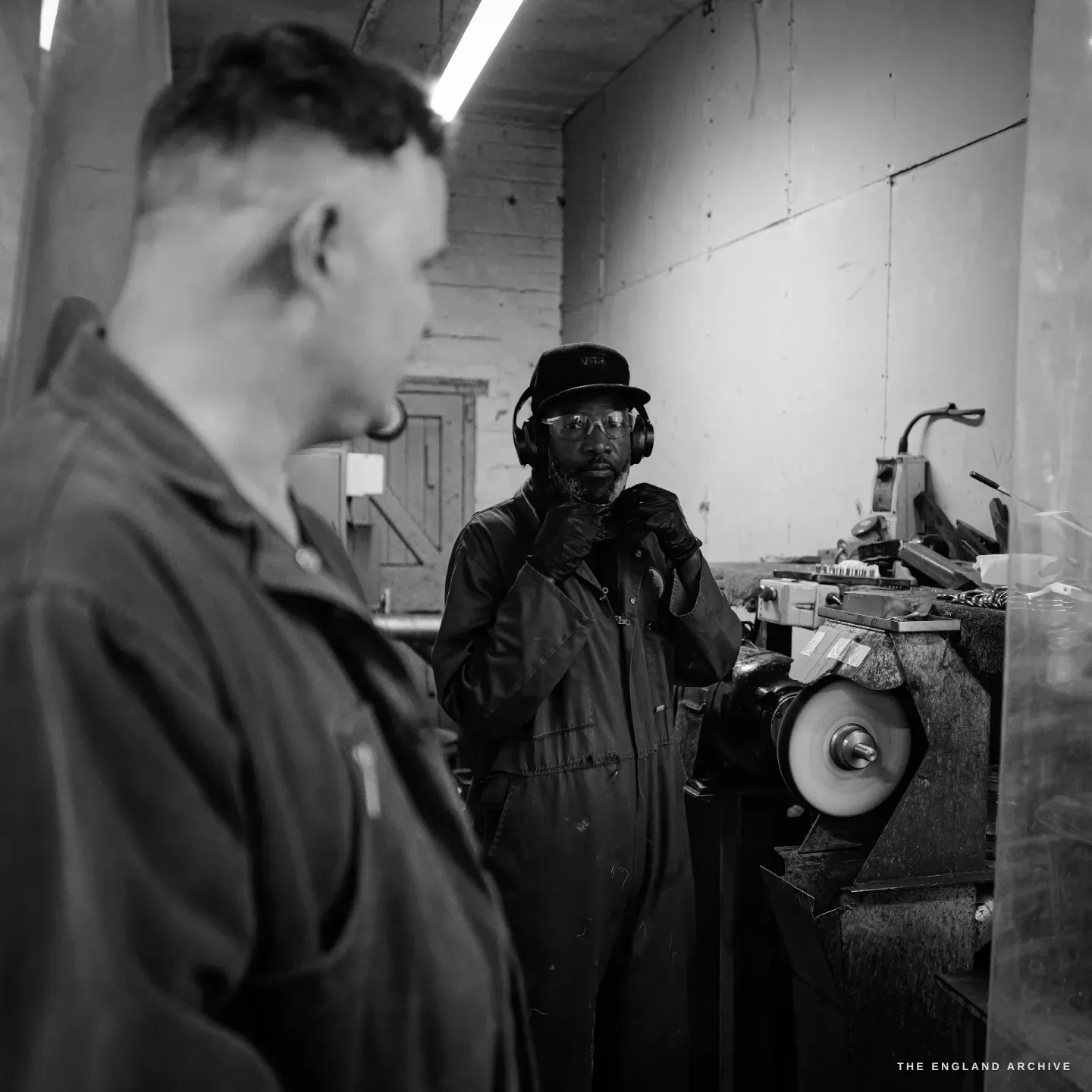 Sabino at his polishing machine in conversation with another maker in the foreground, the white buffing wheel on its spindle beside him.