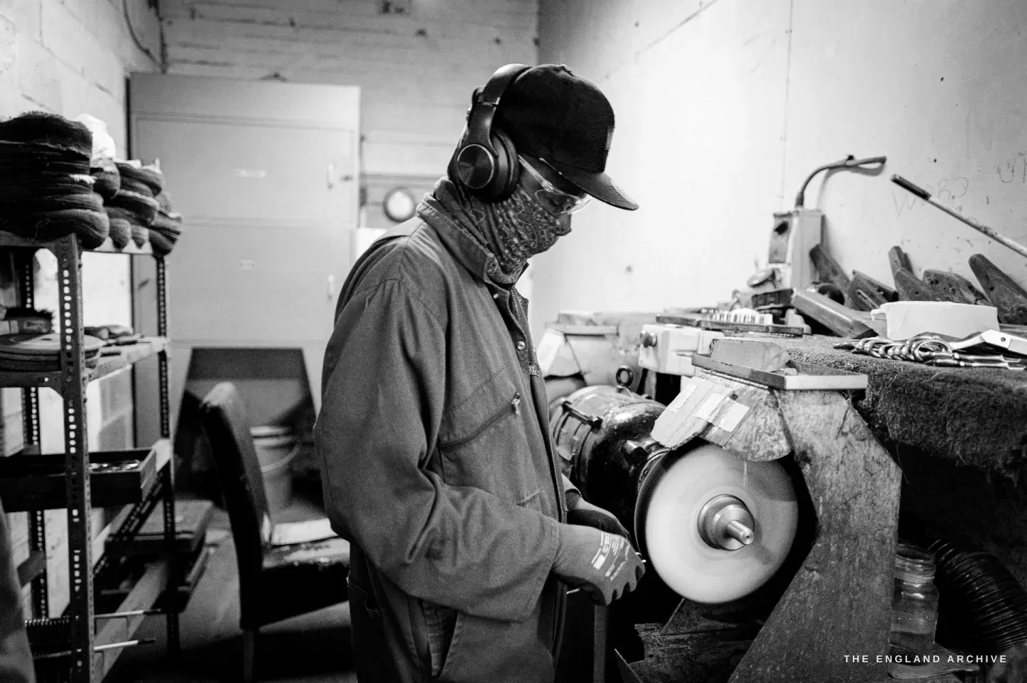 Sabino in profile at the polishing wheel, a scarf pulled up over his nose against the dust, working a pair against the spinning mop.