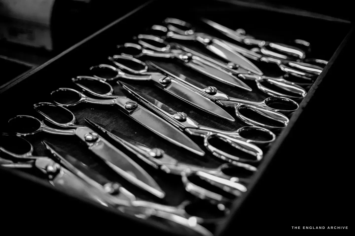A black tray filled with rows of finished bright scissors, blades and bow handles catching the light.