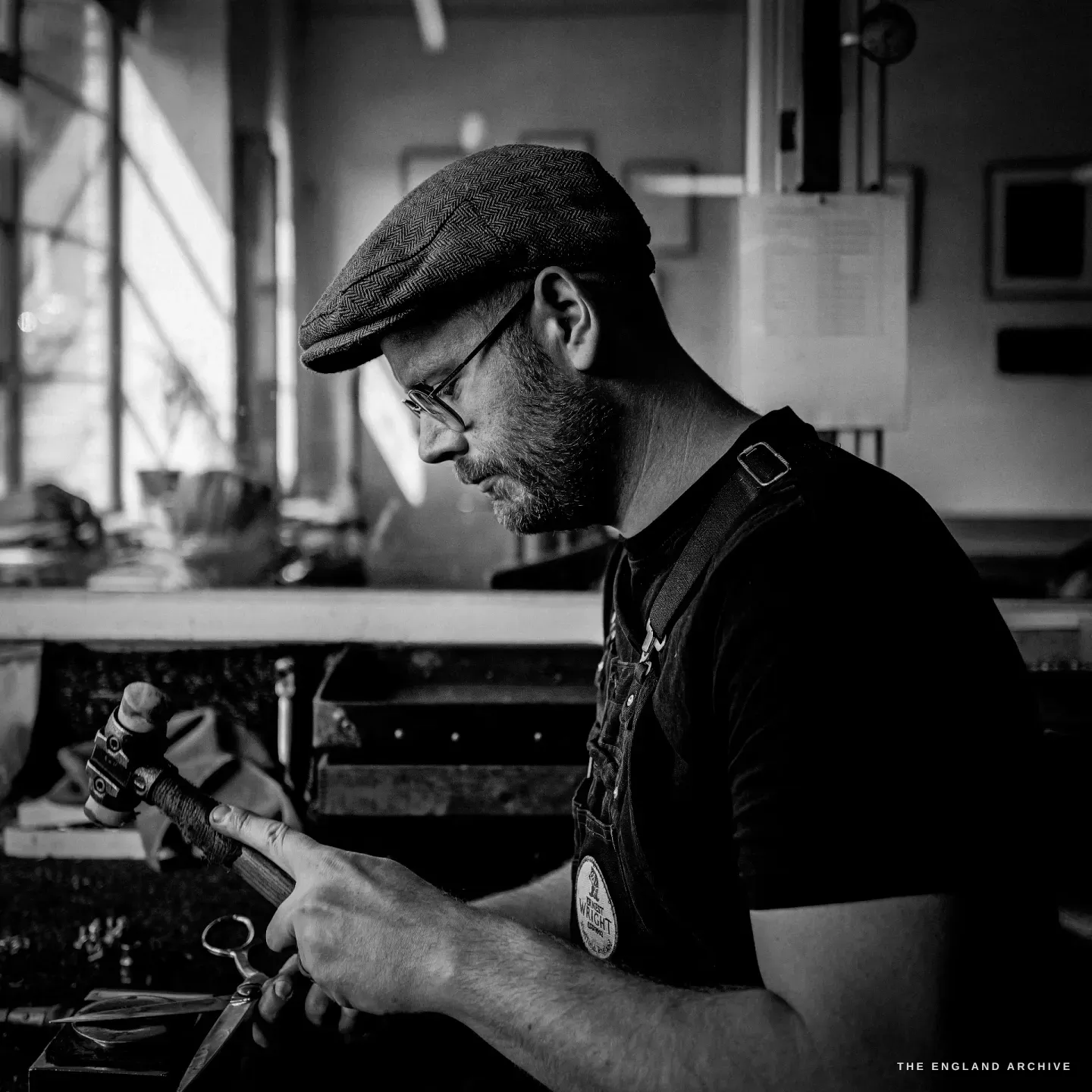 Sam in profile with a hammer in hand, looking down at a pair of scissors, strong side light from the window.