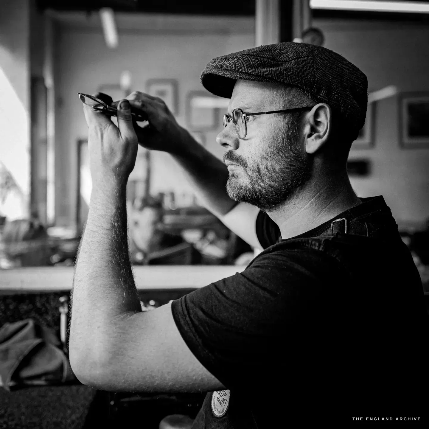 Sam holding a finished pair of scissors up to the window light, sighting through the blades to read the gap between them.