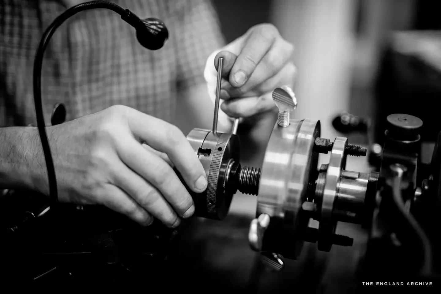 Both of Seth Kennedy’s hands adjusting the rose engine’s index-and-dividing ring with an Allen key, the brass chuck and worm-screw in sharp focus.