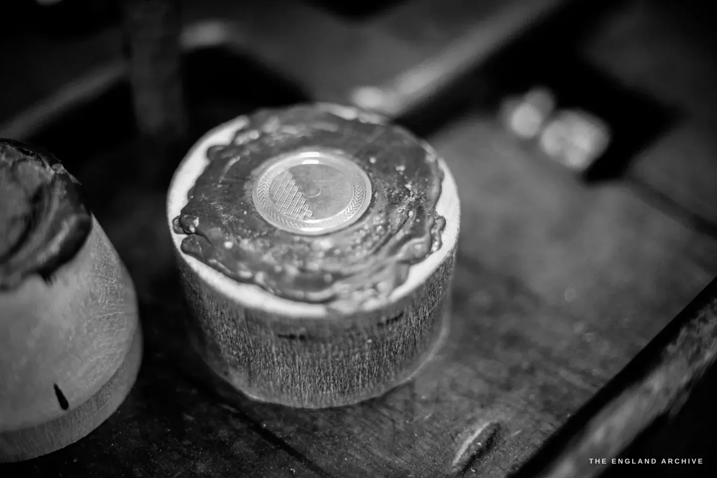 A small disc set in a black pitch-and-shellac chuck on a wooden block - a blank workpiece mounted ready for engine turning.