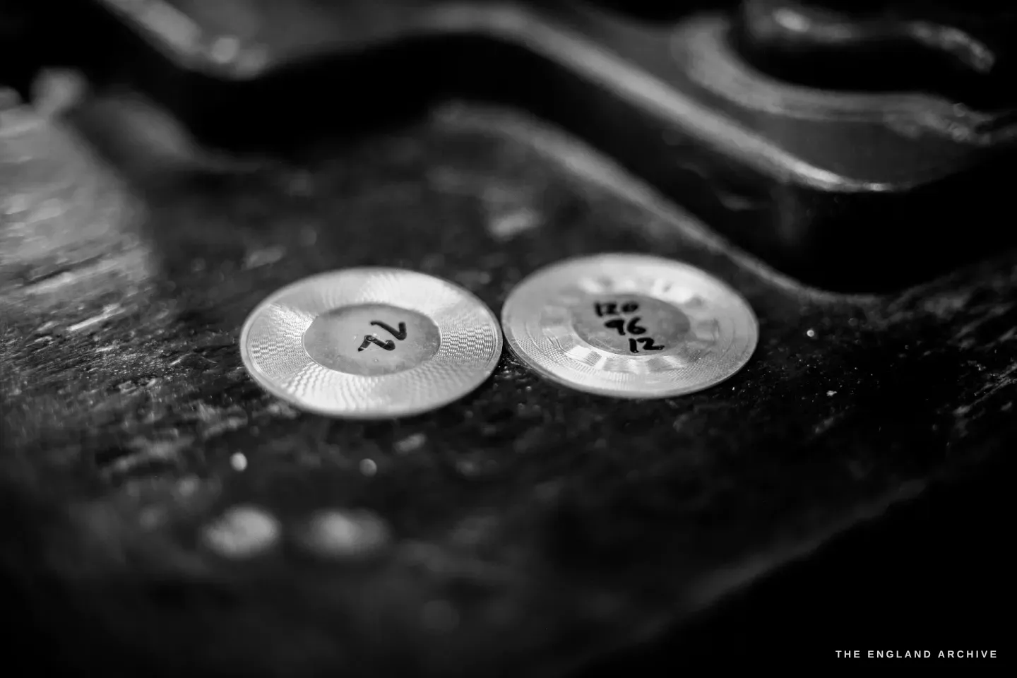 Two engine-turned discs on a dark surface with handwritten ink markings - "72" on one, "120 / 96 / 12" on the other - the division counts.