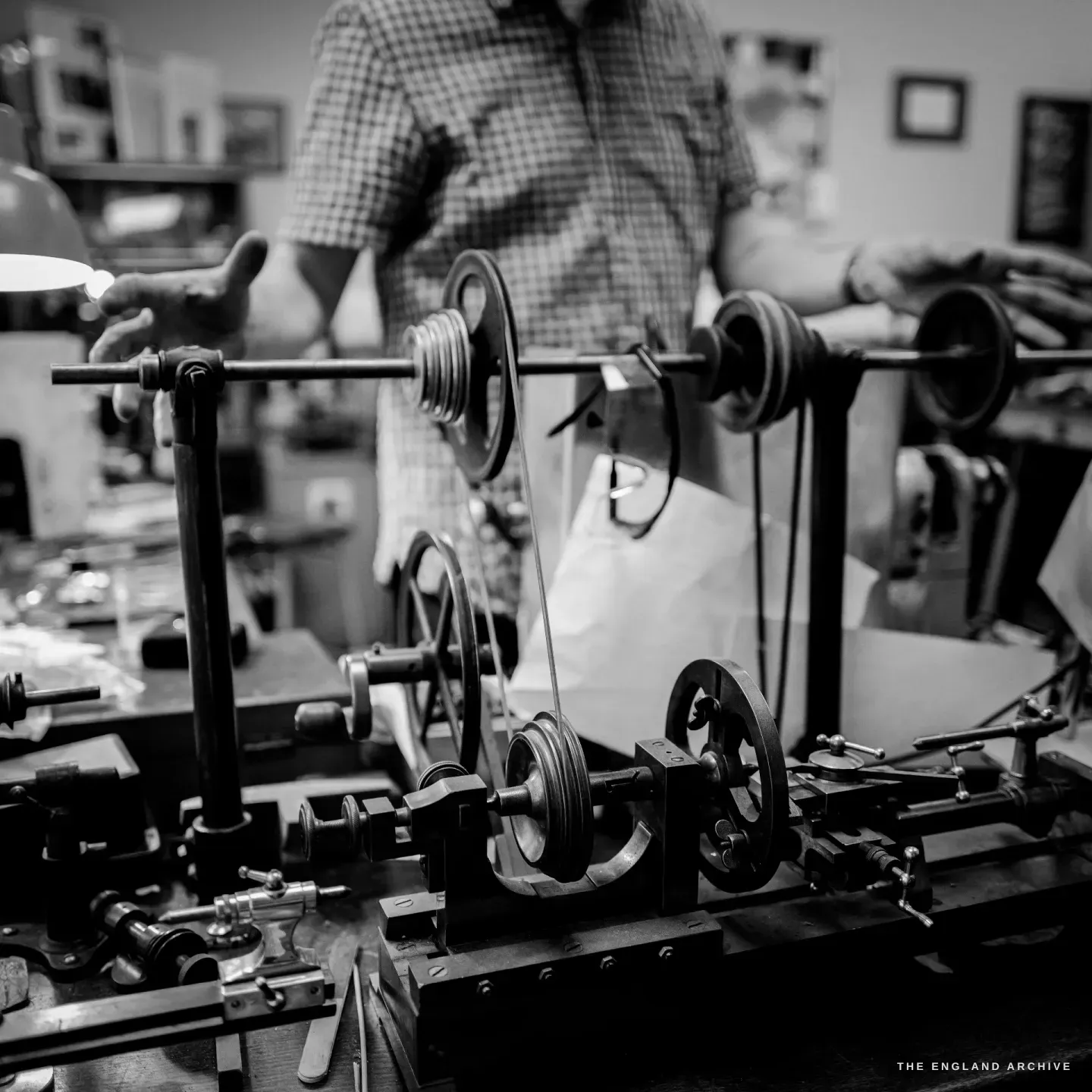 A closer front view of the straight-line engine’s belt drive - the line-shaft, stacked pulley wheels and flywheels on the bed, Seth Kennedy’s torso behind.