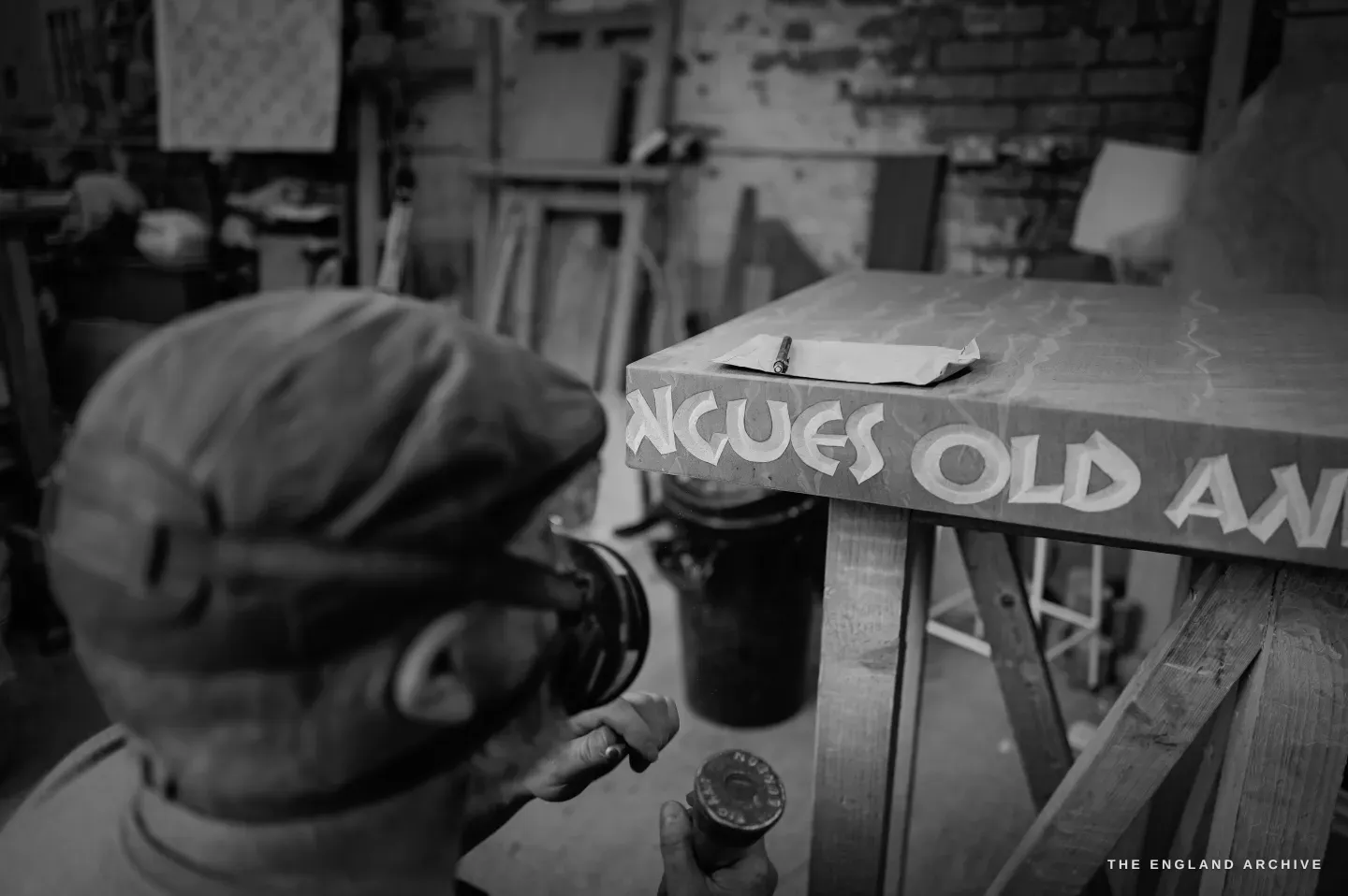 Over Steve Roche’s shoulder as he cuts the words ‘ngues old an…’ into the long stone sign, a round mallet in his fist, his flat cap and the strap of his respirator in the foreground.