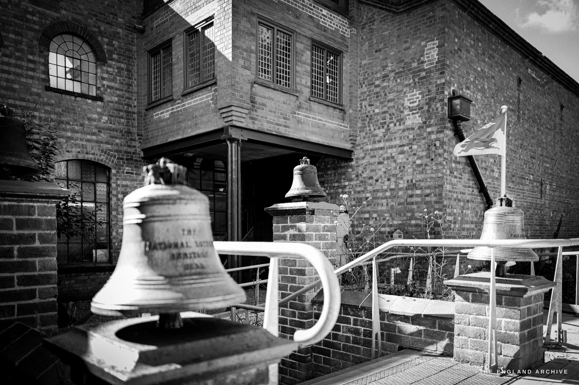 Three bells mounted on brick plinths as outdoor exhibits in the museum courtyard, a flag flying and the brick foundry building behind.