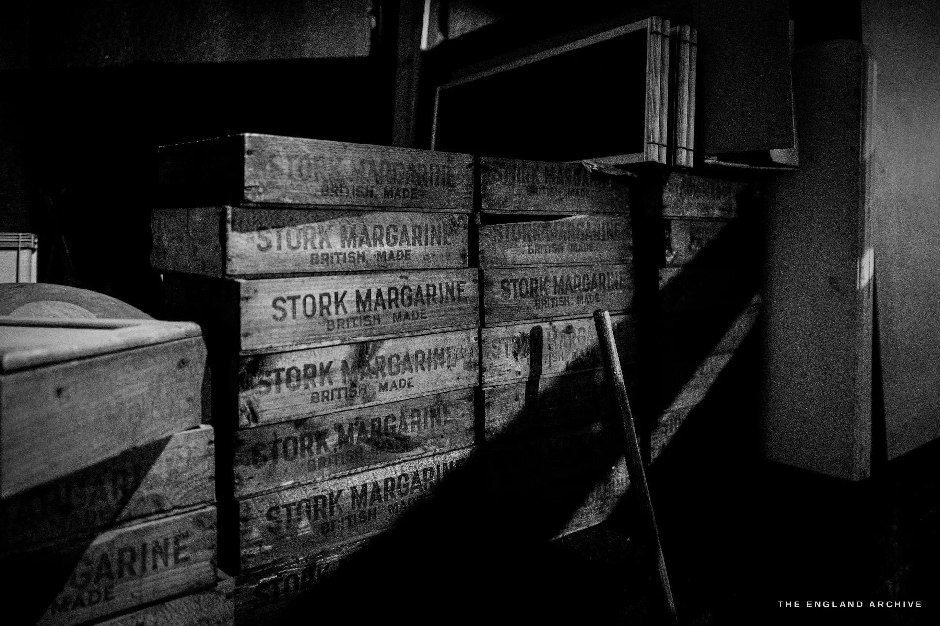 A stack of old wooden packing crates stencilled STORK MARGARINE BRITISH MADE, kept as historic storage in a dim store.