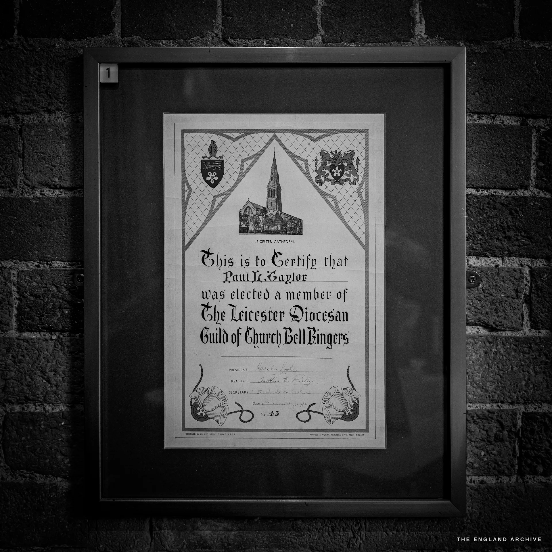 A framed illuminated certificate of membership of the Leicester Diocesan Guild of Church Bell Ringers, with heraldic crests and a drawing of Leicester Cathedral.