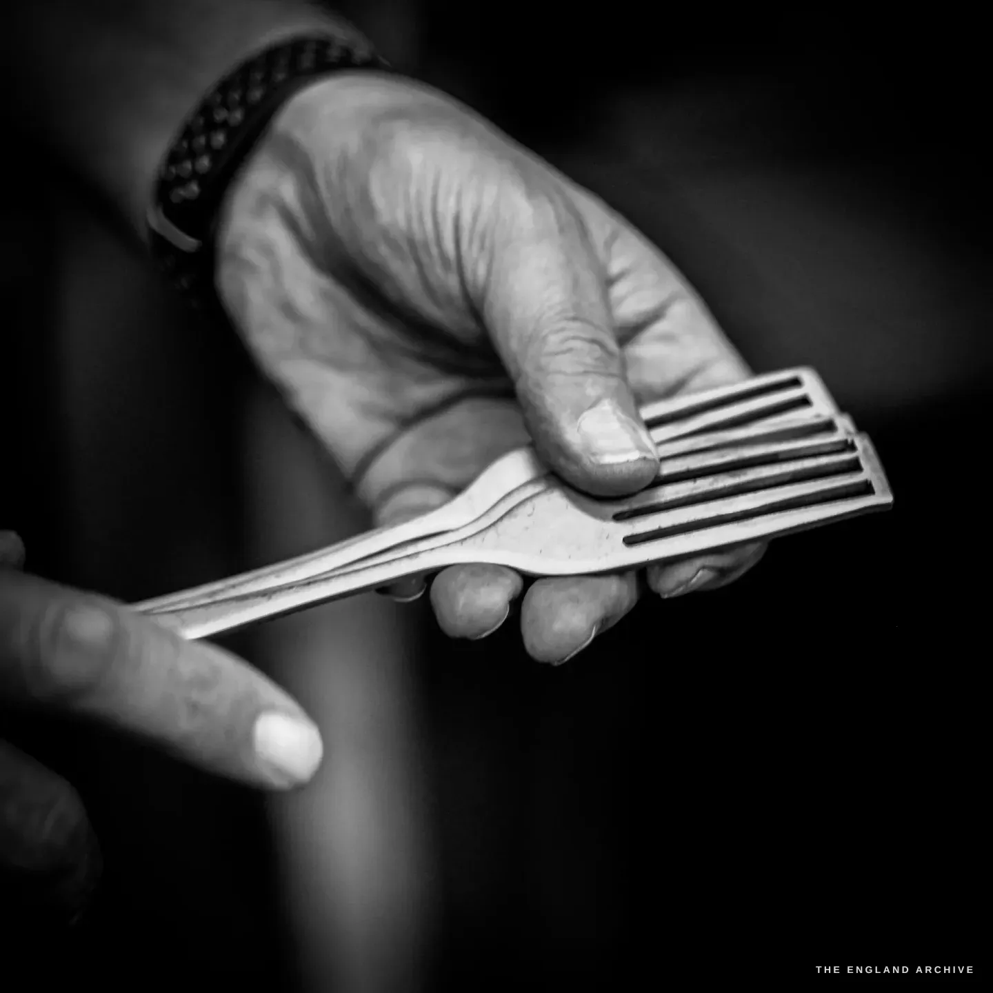 A close view of Stephen Wright’s weathered hand holding a part-made fork, the tines slotted but the blank still flat.