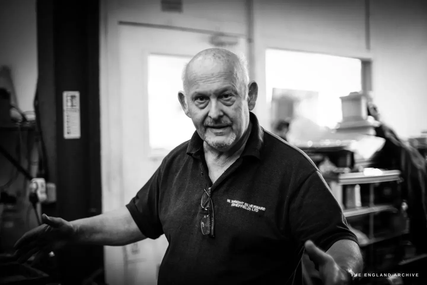 Stephen Wright mid-gesture with both arms spread, talking and smiling in the workshop.