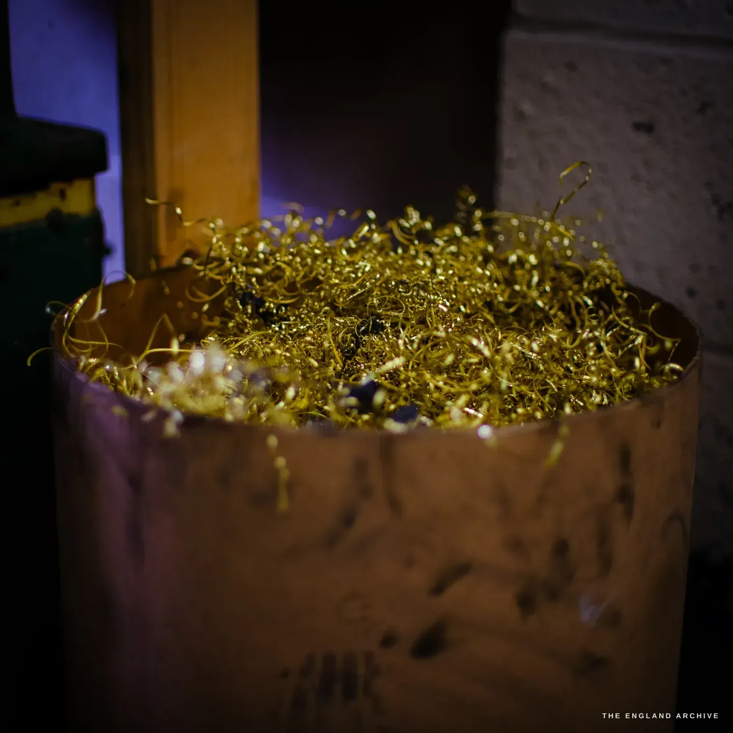 A drum filled with curled golden swarf, the bright metal shavings glowing against the dark of the workshop.