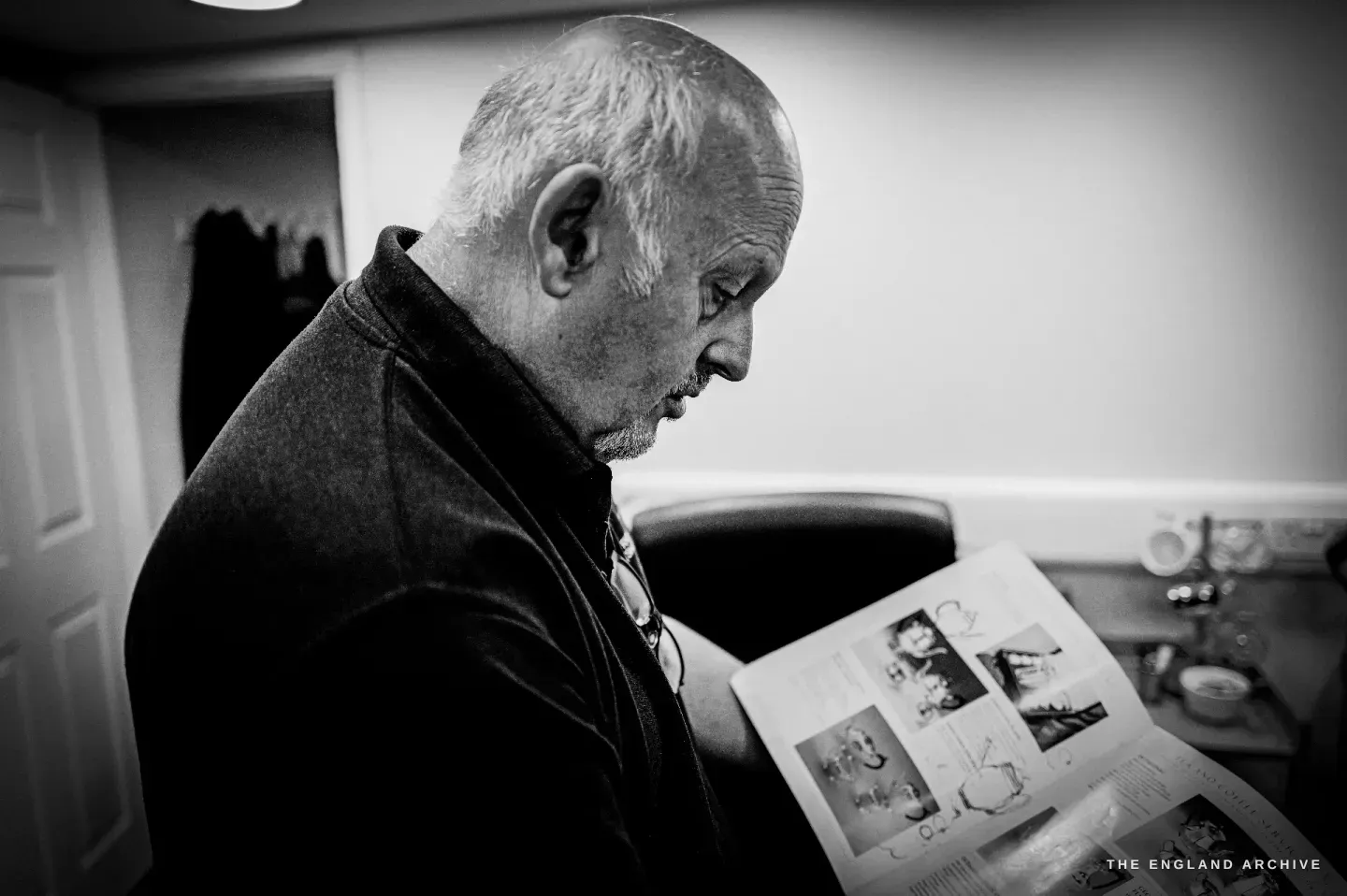 Stephen Wright in the office, head bowed over an open illustrated catalogue, studying the pages.
