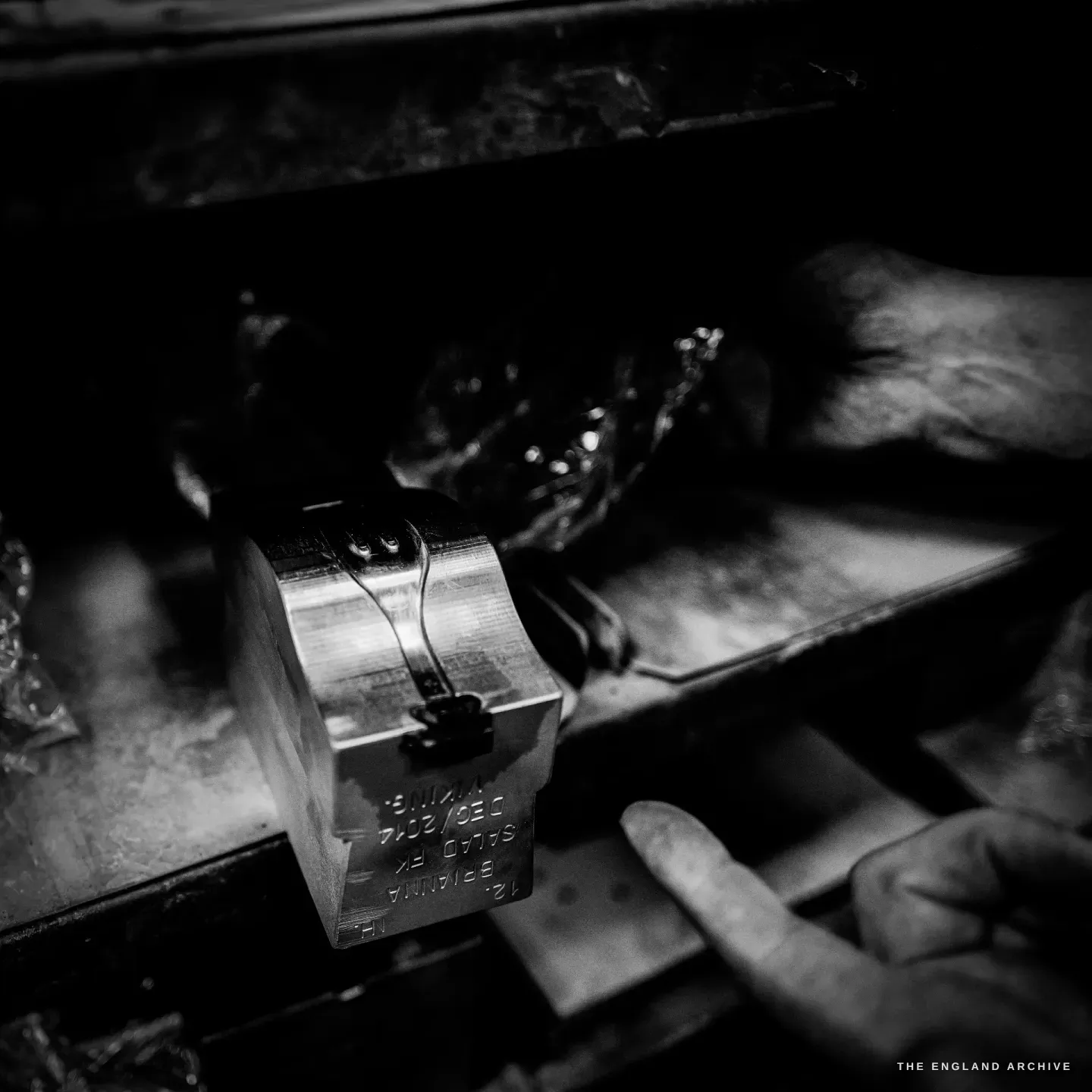 A close view of a steel die block with engraved lettering on its face, a finger resting beside it.